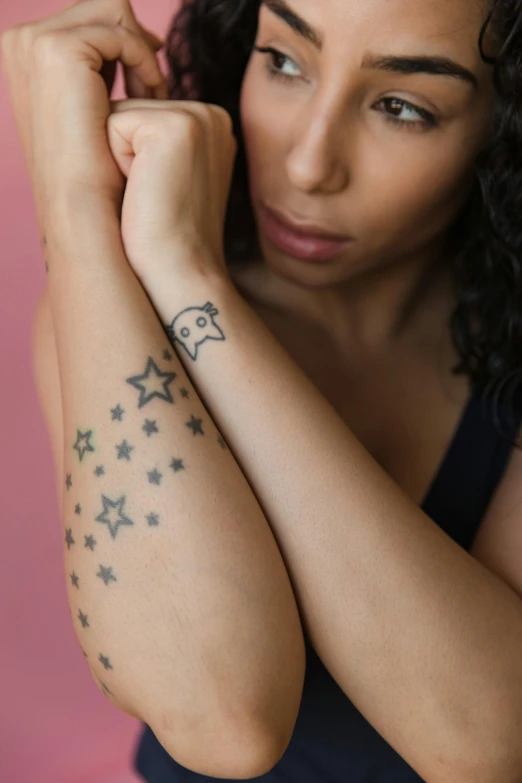 a woman with a tattoo on her arm, trending on pexels, multiple stars visible, with a sad expression, plain background, uncropped