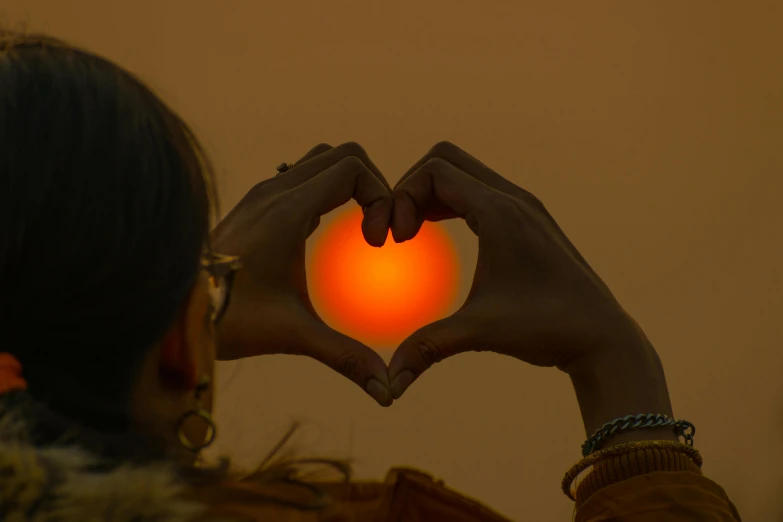 a woman making a heart shape with her hands, by Julia Pishtar, pexels contest winner, glowing magma sphere, (light orange mist), tactile buttons and lights, holding a lantern