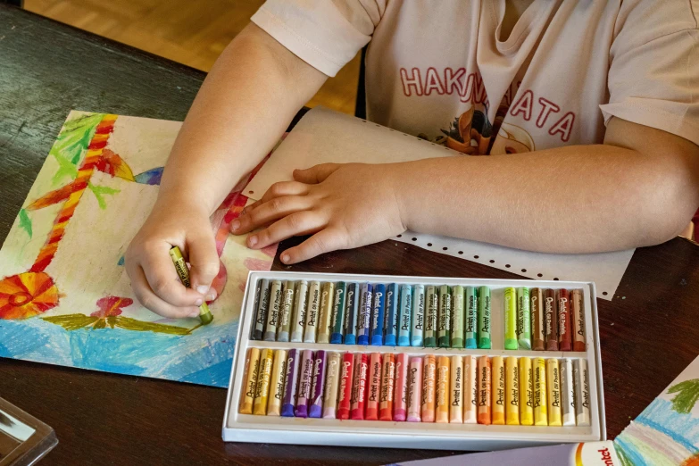 a person sitting at a table with a box of crayons, a child's drawing, inspired by Quentin Blake, pexels contest winner, crayon art, oil pastels and gold, photorealism pastel, instagram post, performing