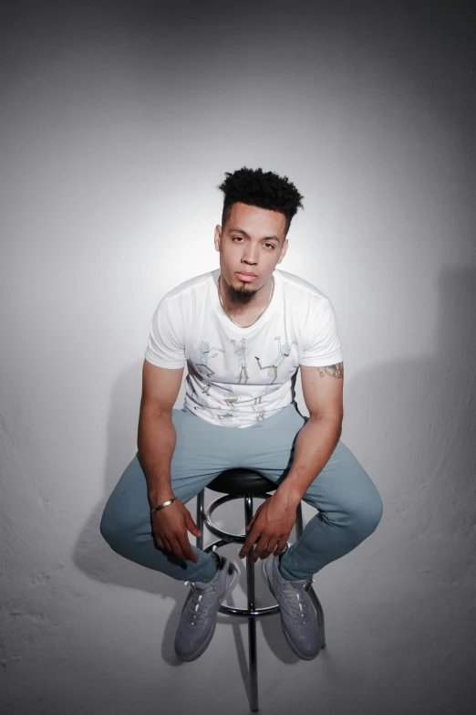 a man sitting on top of a stool, an album cover, by Christopher Williams, trending on pexels, lyco art, dressed in a white t-shirt, charles perry, headshot profile picture, light skin