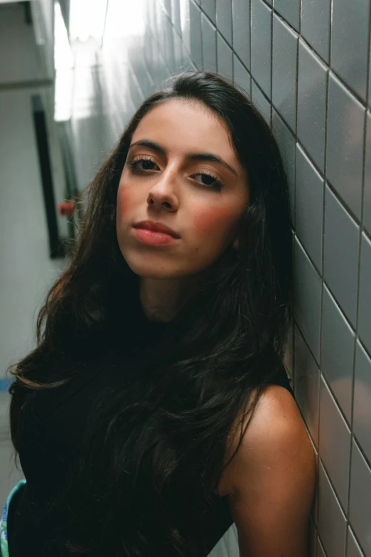 a woman leaning against a wall in a bathroom, an album cover, by Olivia Peguero, antipodeans, standing with a black background, looking serious, promo image, aubrey plaza