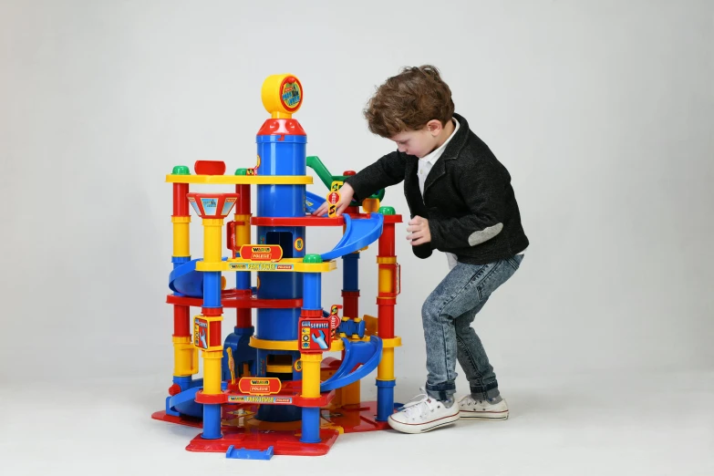 a young boy playing with a toy tower, inspired by Rube Goldberg, instagram, bauhaus, set inside of parking garage, blippi, official product photo, multi colour