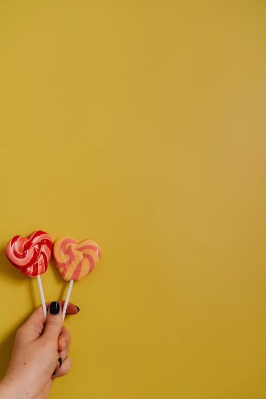 a person holding two lollipops in their hands, pexels contest winner, yellow wallpaper, raspberry banana color, swirl, caramel