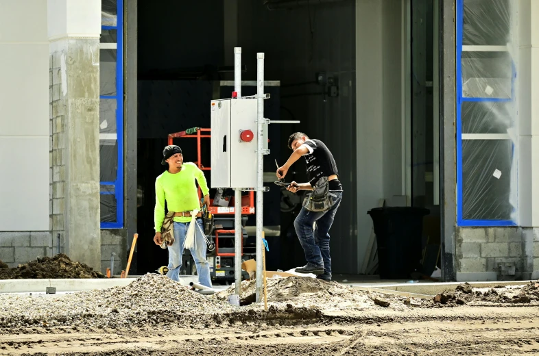a couple of men standing in front of a building, working, on the concrete ground, “gas station photography, avatar image