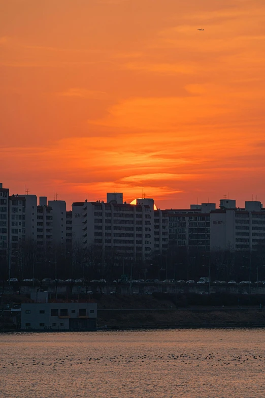 a large body of water with buildings in the background, by Sven Erixson, pexels contest winner, brutalism, orange sun set, pyongyang city, soviet apartment building, panorama