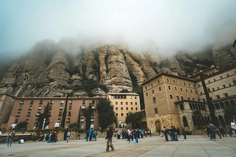 a group of people standing in front of a mountain, inspired by Modest Urgell, pexels contest winner, gothic quarter, monserrat gudiol, under a gray foggy sky, tiny people walking below