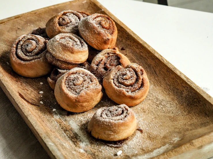 a wooden tray filled with cinnamon rolls covered in powdered sugar, a portrait, trending on pexels, snails, rosen zulu, jen atkin, 🎀 🧟 🍓 🧚