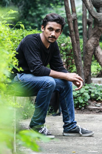 a man sitting on a bench in a park, inspired by Sunil Das, wearing a dark shirt and jeans, with mustache, serious look, raden saleh