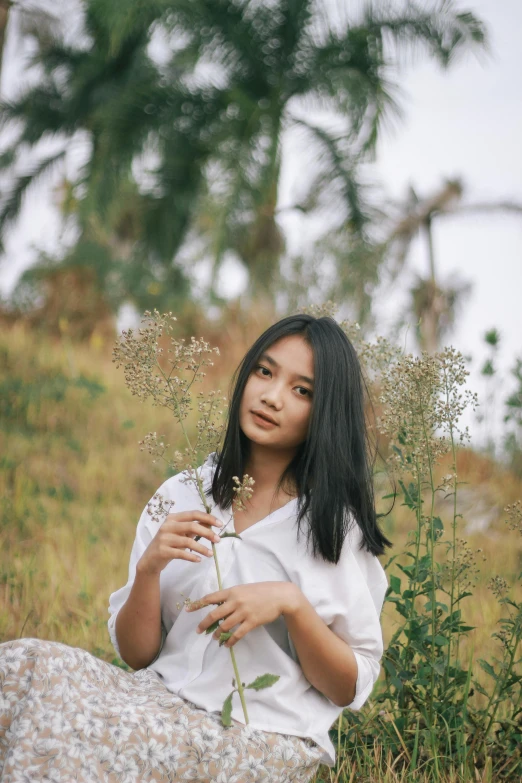 a woman sitting in a field holding a flower, a picture, by Tan Ting-pho, unsplash, realism, 🤤 girl portrait, with straight black hair, medium format, 1 6 years old