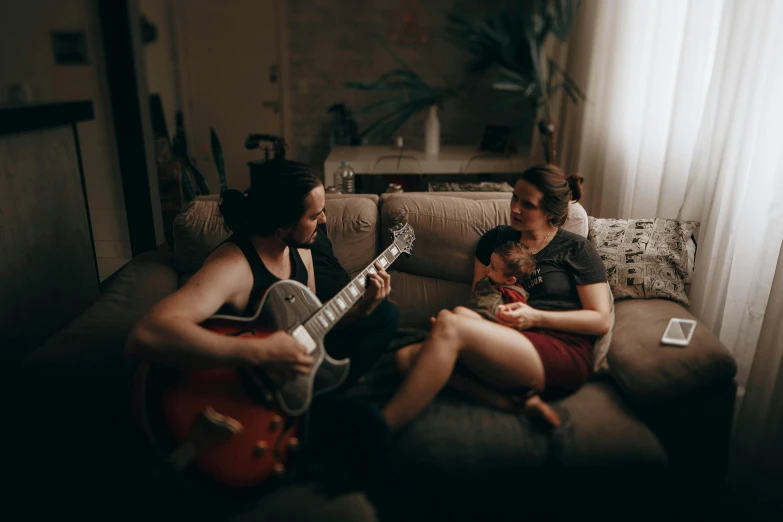 a couple of people that are sitting on a couch, an album cover, by Lee Loughridge, pexels contest winner, happening, husband wife and son, playing electric guitar, jovana rikalo, evening time