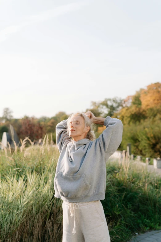 a woman standing on top of a sidewalk next to tall grass, trending on unsplash, happening, wearing silver hair, wearing sweatshirt, arms raised, portrait of elle fanning