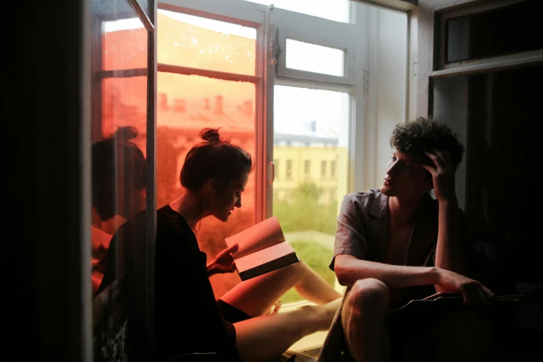 a couple of people sitting in front of a window, by Zofia Stryjenska, pexels contest winner, book library studying, light red and orange mood, high school, summer afternoon