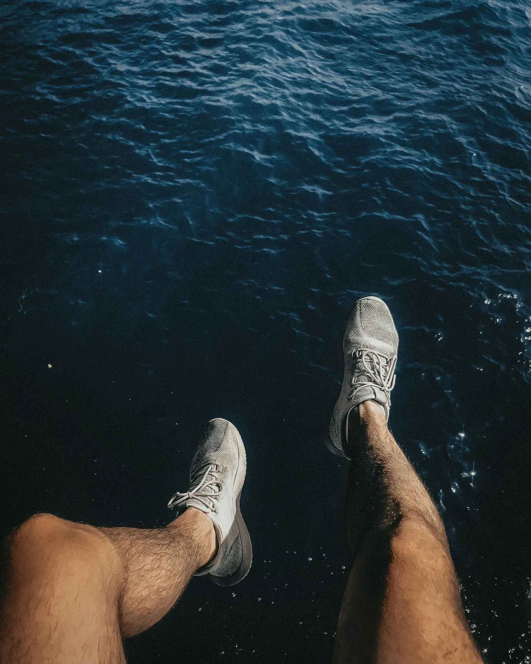a man sitting on top of a boat next to a body of water, by Adam Dario Keel, pexels contest winner, gray shorts and black socks, two male, legs taking your pov, wearing white sneakers