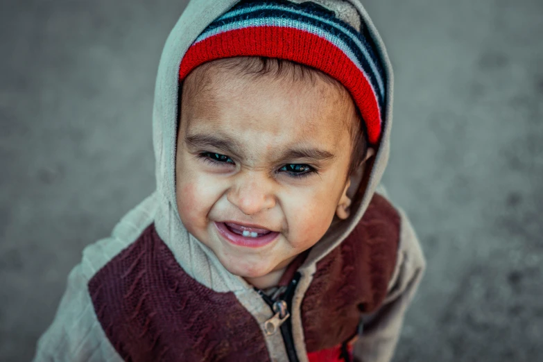 a close up of a child wearing a hoodie, by Ibrahim Kodra, pexels contest winner, hurufiyya, angry smile, toddler, with a hurt expression, colour corrected