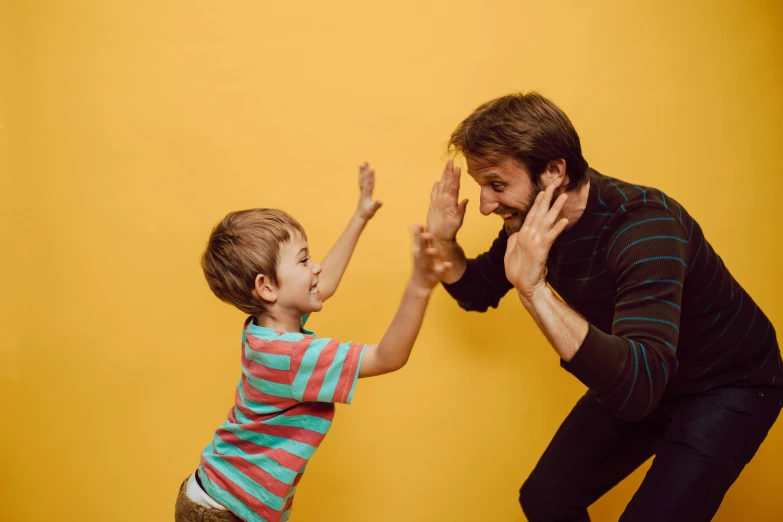 a man standing next to a little boy in front of a yellow wall, pexels contest winner, interactive art, dancing with each other, plain background, brown, promotional image