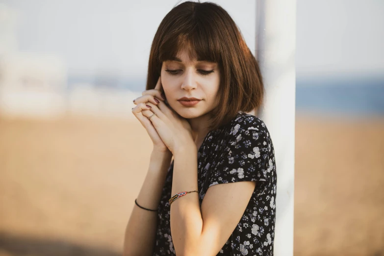 a woman leaning against a pole on the beach, trending on pexels, short brown hair with bangs, portrait of depressed teen, hands on face, stylised