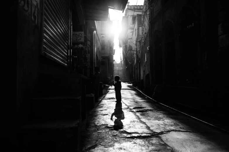 a black and white photo of a person walking down a street, by Ahmed Yacoubi, pexels contest winner, light over boy, cairo, the girl and the sun, streets of calcutta