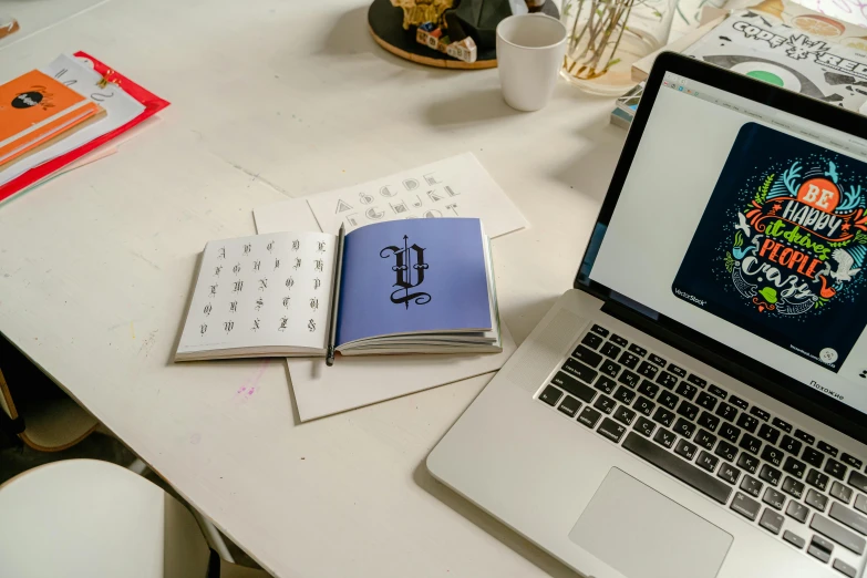 a laptop computer sitting on top of a white desk, by Carey Morris, letterism, blue print, thumbnail, ornate designs on desk, holding notebook