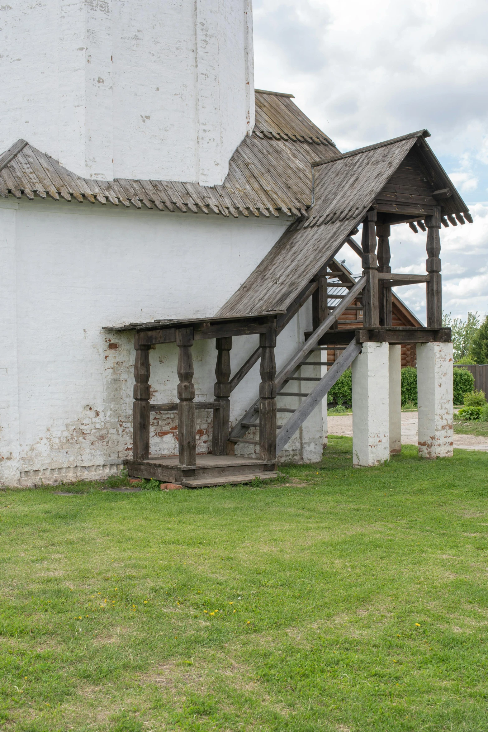 a white building sitting on top of a lush green field, inspired by Konstantin Vasilyev, renaissance, wooden stairs, rustic setting, rutkowskyi, seen from the side