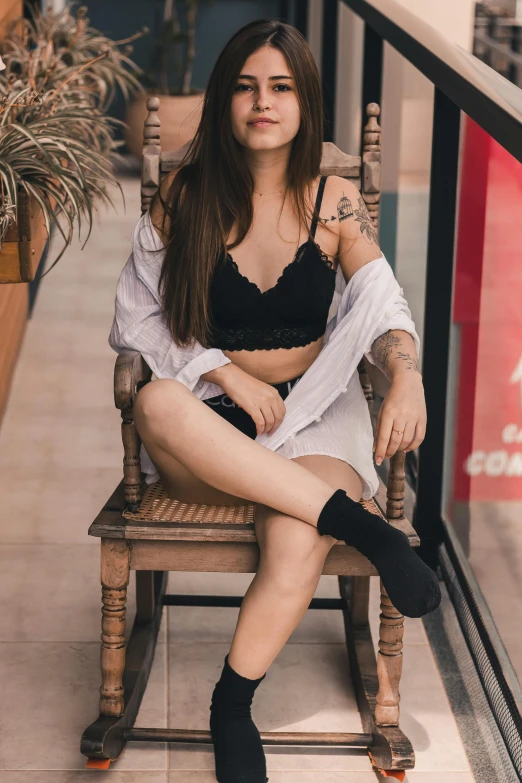 a woman sitting on top of a wooden chair, a tattoo, inspired by Elsa Bleda, pexels contest winner, renaissance, bra and shorts streetwear, beautiful young asian woman, black bra, young teen