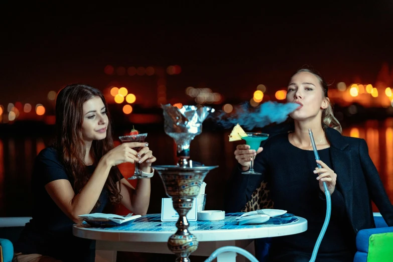 two women sitting at a table smoking a hook, by Julia Pishtar, shutterstock, hurufiyya, cocktail bar, arabian nights inspired, at the waterside, blue