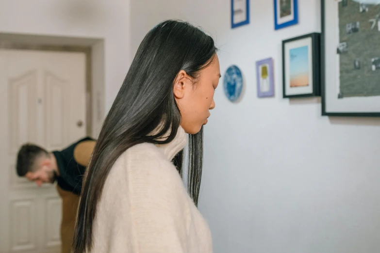 a woman standing next to a man in a living room, a minimalist painting, inspired by helen huang, pexels contest winner, black haired girl wearing hoodie, gallery display photograph, close - up profile, acupuncture treatment