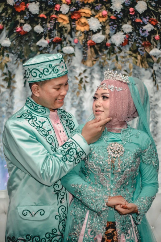 a man and a woman standing next to each other, a colorized photo, by Basuki Abdullah, pexels contest winner, hurufiyya, big crown adorned with emerald, glittery wedding, white and teal garment, thumbnail