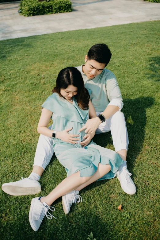 a man and a woman sitting on the grass, set on singaporean aesthetic, maternity feeling, with teal clothes, arm around her neck