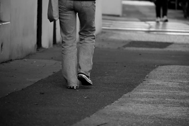 a person walking down a sidewalk with an umbrella, a black and white photo, blue jeans and grey sneakers, taken with my nikon d 3, stripey pants, dof narrow