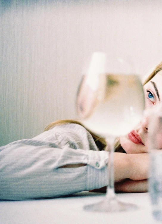 a woman sitting at a table with a glass of water, inspired by Elsa Bleda, trending on unsplash, aestheticism, lying in bed, intricate heterochromia sad, overexposed photograph, movie still of a tired