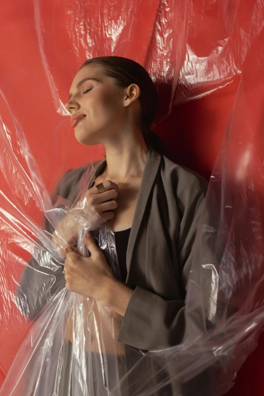 a woman wrapped in plastic in front of a red wall, inspired by Anna Füssli, shutterstock contest winner, promo still, fluid bag, in a claustrophobic, promotional photo