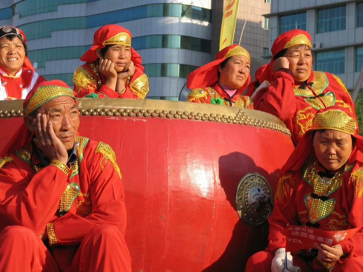 a group of people sitting on top of a red drum, inspired by Nam Gye-u, pexels contest winner, cloisonnism, parade setting, late morning, reflecting, red suit