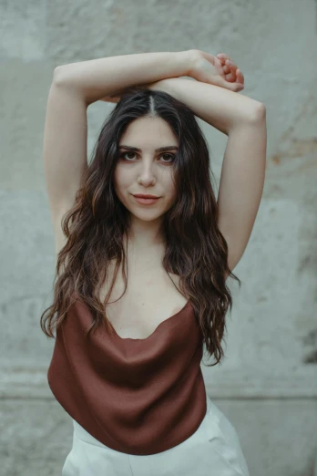 a woman posing in front of a stone wall, an album cover, inspired by Elsa Bleda, trending on pexels, renaissance, beautiful jewish woman, armpit, brown hair flow, wearing a tanktop