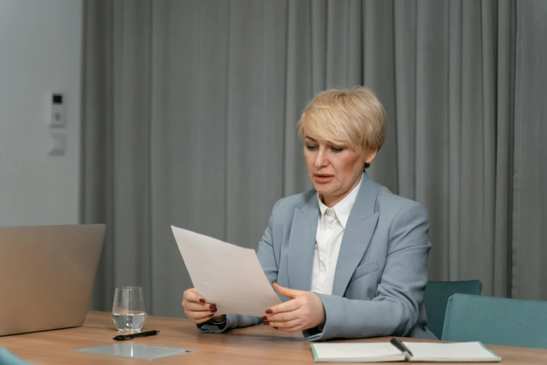 a woman sitting at a table in front of a laptop, court session images, high quality paper, realistic », a blond