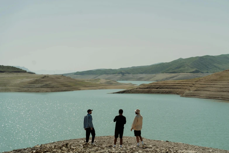 three men standing at the edge of a large body of water, an album cover, pexels contest winner, hurufiyya, mesopotamic, mountain lakes, still from a music video, water reservoir