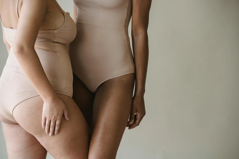 a couple of women standing next to each other, by Emma Andijewska, trending on pexels, renaissance, muted colored bodysuit, her skin is light brown, thicc, silicone skin