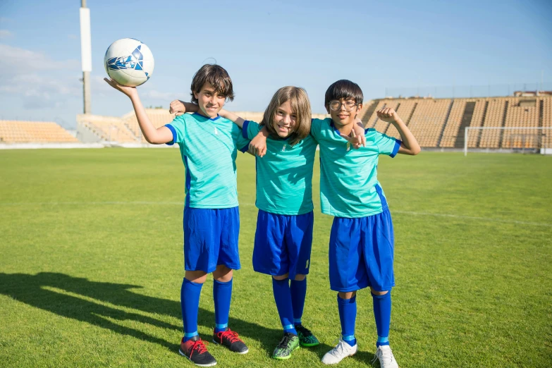 three children posing for a picture with a soccer ball, a picture, shutterstock, danube school, teal uniform, egypt, thumbnail, sunny day time