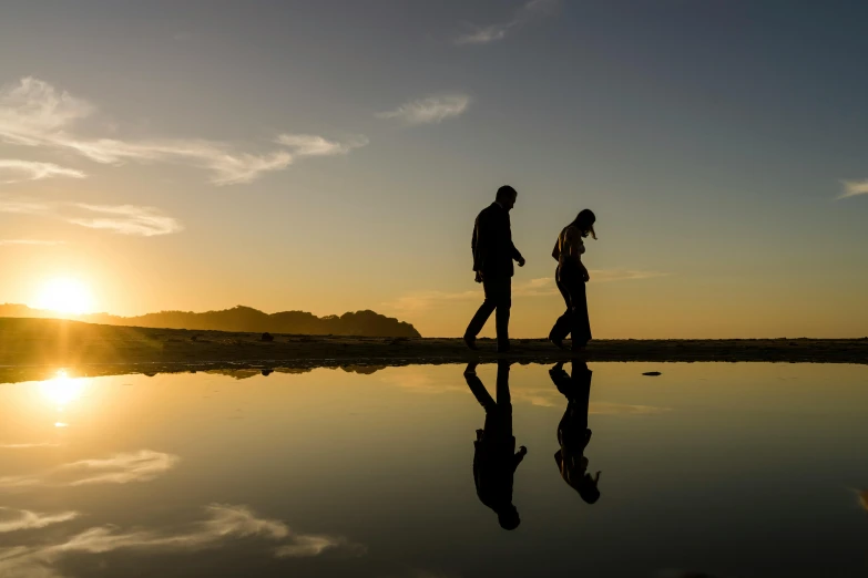 a man and a woman walking on a beach at sunset, by Lee Loughridge, pexels contest winner, mirror reflections, golden bay new zealand, reflective ground, detailed silhouette