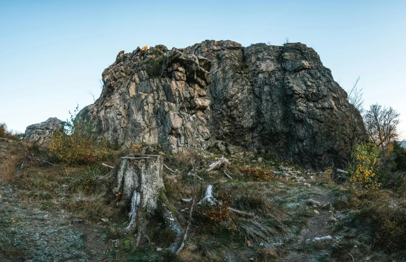 a large rock sitting on top of a grass covered hillside, by Jesper Knudsen, unsplash, tree stumps, rock quarry location, 4 k cinematic panoramic view, high-quality photo