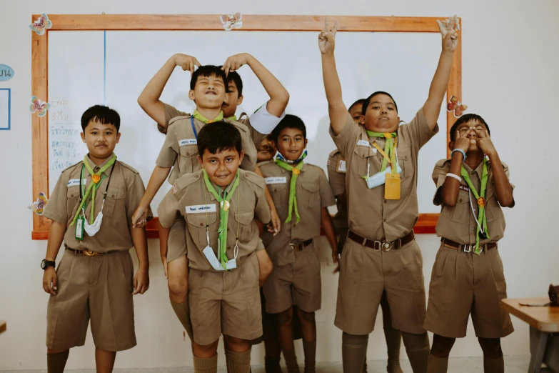 a group of young boys standing in front of a whiteboard, pexels contest winner, sumatraism, boy scout troop, background image, brown clothes, pose(arms up + happy)