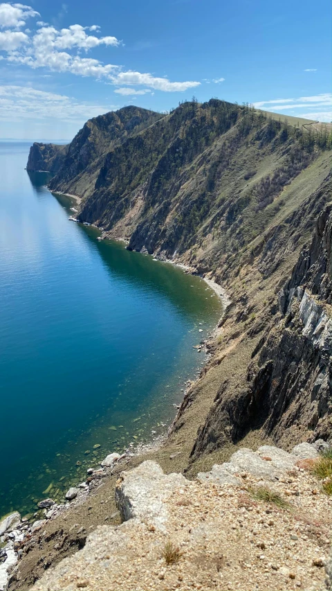 a man standing on top of a cliff next to a body of water, near lake baikal, slide show, single file, feature