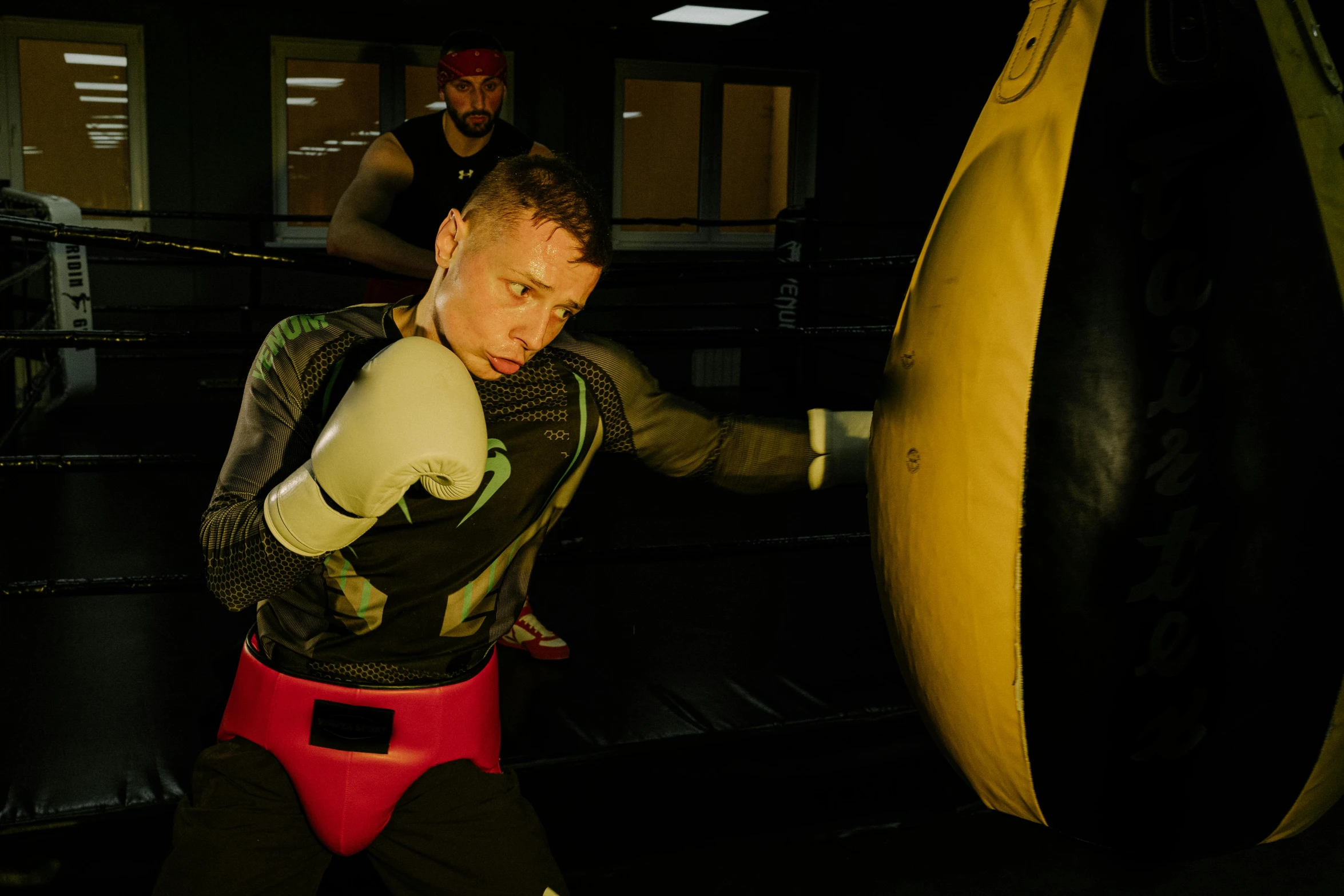 a man in a boxing ring with a punching bag, a portrait, pexels contest winner, black and yellow tracksuit, ryan renolds as batman, liam brazier and nielly, working out