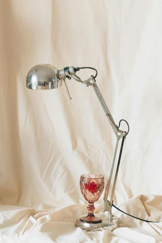 a lamp sitting on top of a table next to a wine glass, a still life, inspired by Méret Oppenheim, unsplash, photorealism, silver insect legs, mechanical arm, 1990s photograph, poppy