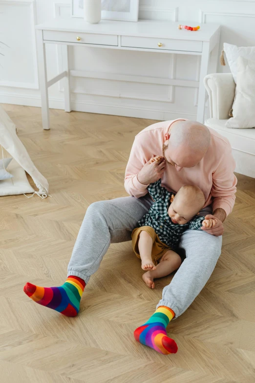 a man sitting on the floor holding a baby, inspired by Okuda Gensō, pexels contest winner, bald on top, socks, old and young, fighting