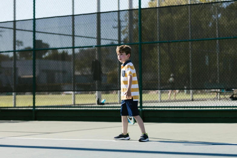 a young boy standing on a tennis court holding a racquet, unsplash, american barbizon school, shot on sony a 7 iii, walking towards camera, various posed, recreation