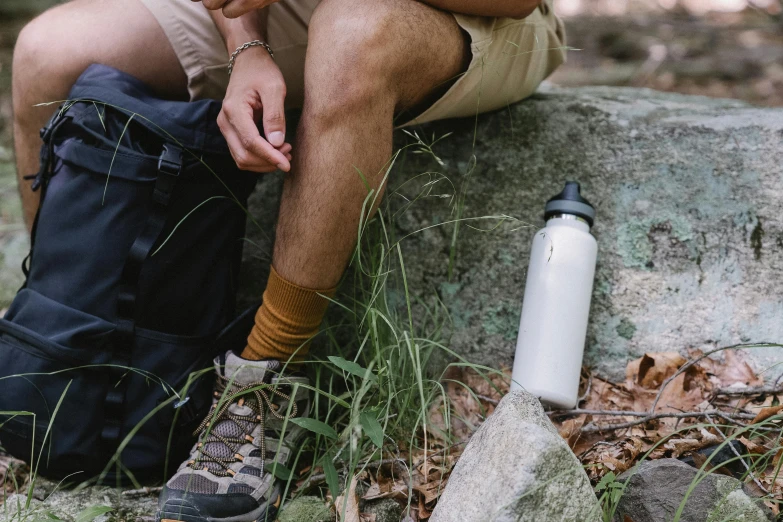 a man sitting on a rock next to a water bottle, foliage clothing, swollen veins, graeme base, easy to use