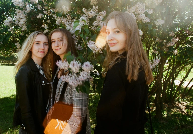 three women standing next to each other in front of a tree, an album cover, by Emma Andijewska, pexels contest winner, happening, flowers on heir cheeks, yulia nevskaya, college, concert