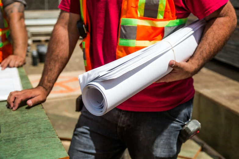 a man holding a roll of paper on top of a table, civil engineer, worksafe. instagram photo, promo image, thumbnail