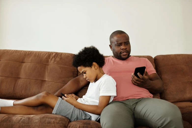 a man and a woman sitting on a couch looking at a cell phone, pexels, father with child, black teenage boy, 15081959 21121991 01012000 4k, struggling