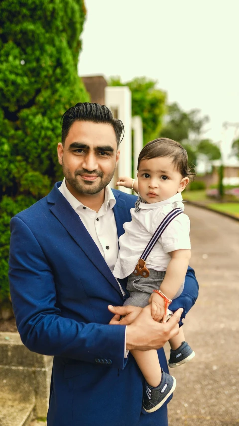 a man in a blue suit holding a baby, by Manjit Bawa, pexels contest winner, hurufiyya, portrait of a handsome, 15081959 21121991 01012000 4k, flat colour, instagram picture